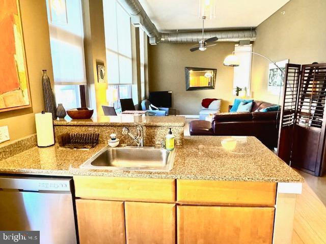 kitchen featuring kitchen peninsula, light stone counters, stainless steel dishwasher, ceiling fan, and sink