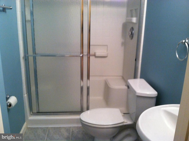 bathroom featuring toilet, a shower with door, and tile patterned flooring