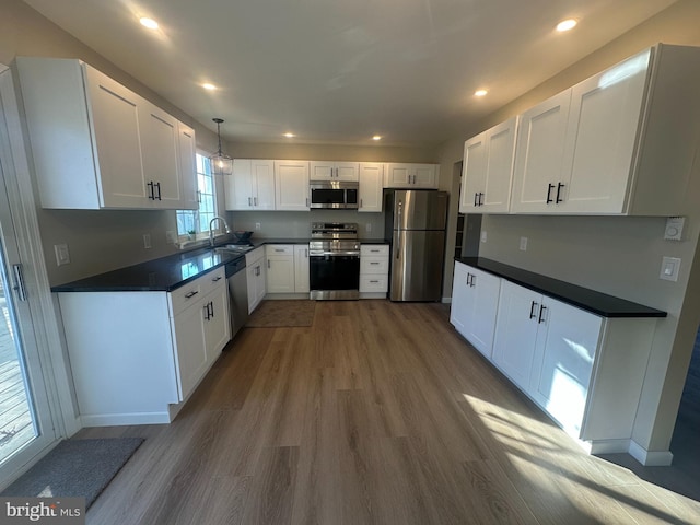 kitchen featuring white cabinets, sink, hardwood / wood-style flooring, appliances with stainless steel finishes, and decorative light fixtures