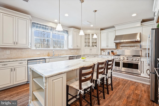 kitchen featuring stainless steel appliances, decorative light fixtures, a center island, a kitchen bar, and ventilation hood