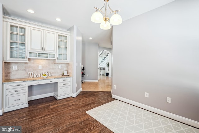 kitchen featuring built in desk, dark hardwood / wood-style flooring, white cabinetry, decorative light fixtures, and tasteful backsplash