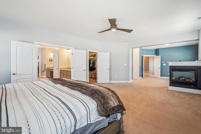 carpeted bedroom featuring a spacious closet, a closet, connected bathroom, a multi sided fireplace, and ceiling fan