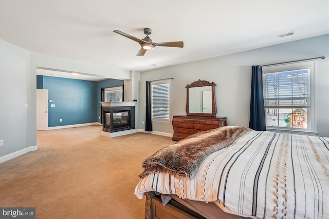 bedroom with ceiling fan, a multi sided fireplace, and light carpet