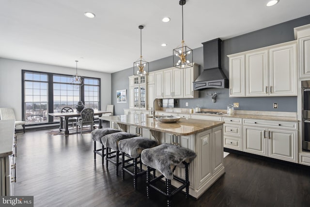 kitchen featuring hanging light fixtures, stainless steel gas cooktop, a kitchen bar, a kitchen island with sink, and custom range hood