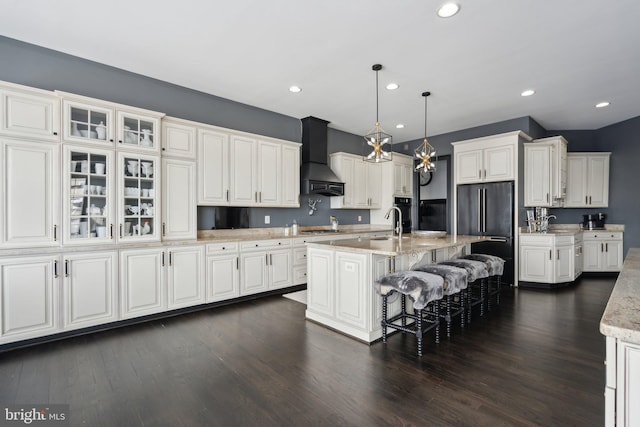 kitchen featuring premium range hood, stainless steel appliances, white cabinets, hanging light fixtures, and an island with sink