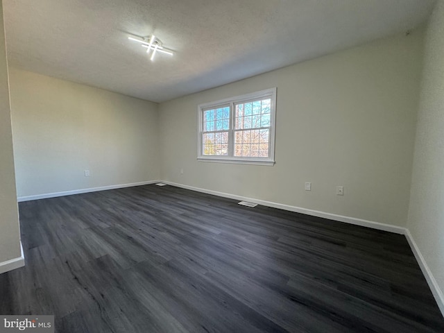 empty room with a textured ceiling and dark hardwood / wood-style flooring