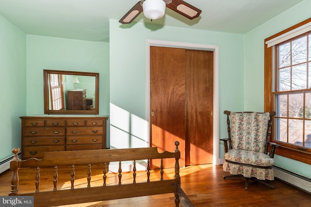 bedroom with ceiling fan, wood-type flooring, and a baseboard heating unit