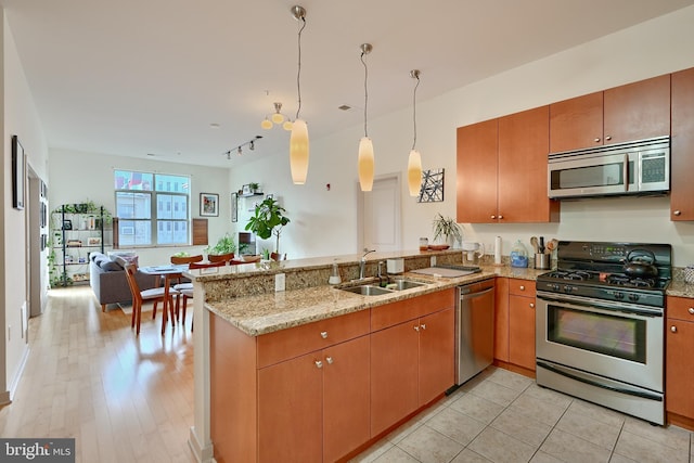 kitchen with sink, decorative light fixtures, light stone counters, kitchen peninsula, and stainless steel appliances