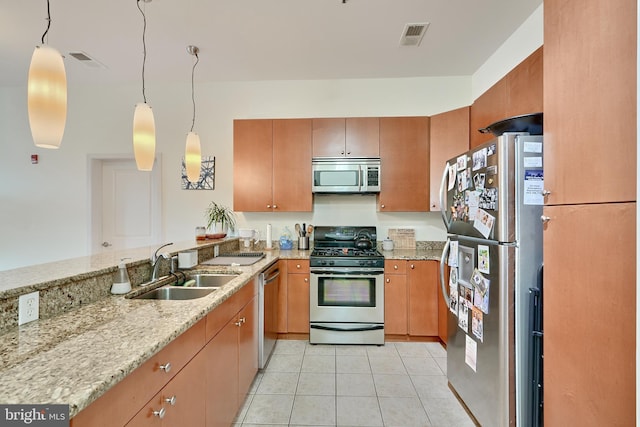 kitchen featuring sink, hanging light fixtures, light tile patterned floors, appliances with stainless steel finishes, and light stone counters