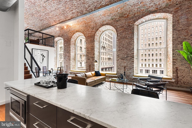 kitchen featuring stainless steel microwave, a high ceiling, wood finished floors, brick ceiling, and baseboards