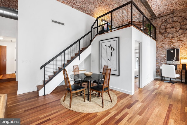 dining area featuring visible vents, baseboards, a towering ceiling, hardwood / wood-style floors, and brick ceiling