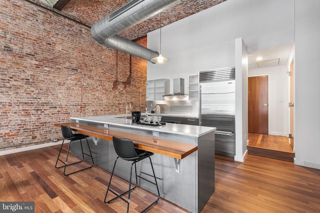 kitchen featuring wall chimney exhaust hood, a high ceiling, built in refrigerator, and dark wood-type flooring