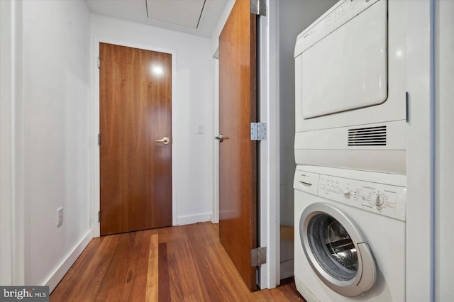 laundry area with laundry area, stacked washer / dryer, wood finished floors, and baseboards