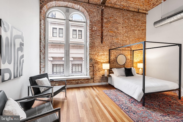 bedroom featuring brick wall, a high ceiling, multiple windows, and wood finished floors