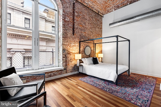 bedroom featuring a high ceiling, brick wall, wood finished floors, brick ceiling, and baseboards