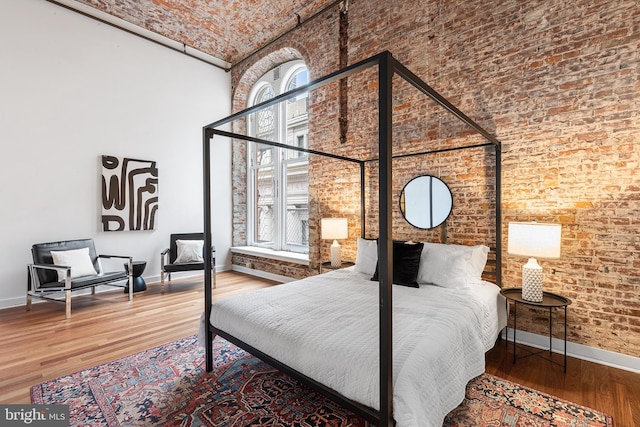 bedroom with a towering ceiling, multiple windows, baseboards, and wood finished floors