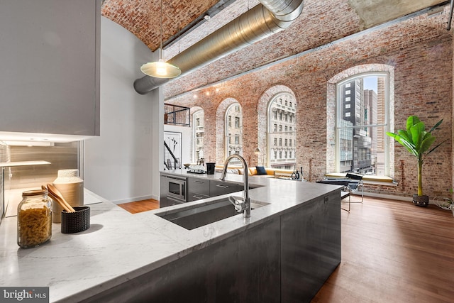 kitchen featuring wood finished floors, a sink, a towering ceiling, brick ceiling, and baseboards