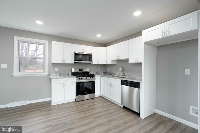 kitchen featuring light stone countertops, appliances with stainless steel finishes, light wood-type flooring, sink, and white cabinetry