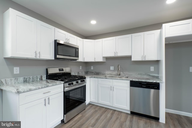 kitchen with light stone countertops, stainless steel appliances, sink, light hardwood / wood-style floors, and white cabinetry