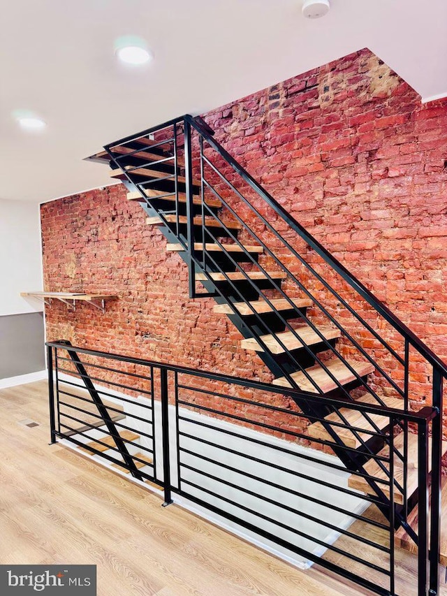 stairway featuring hardwood / wood-style flooring and brick wall