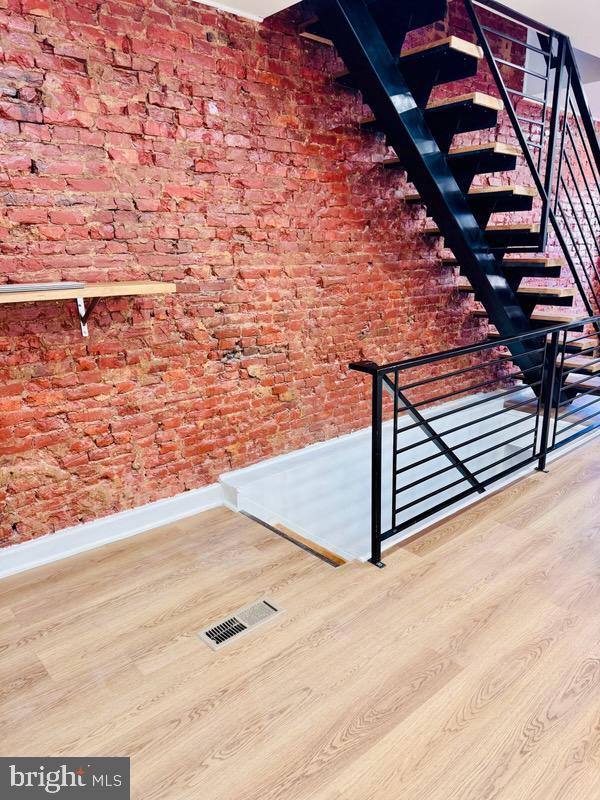 stairs with hardwood / wood-style flooring and brick wall