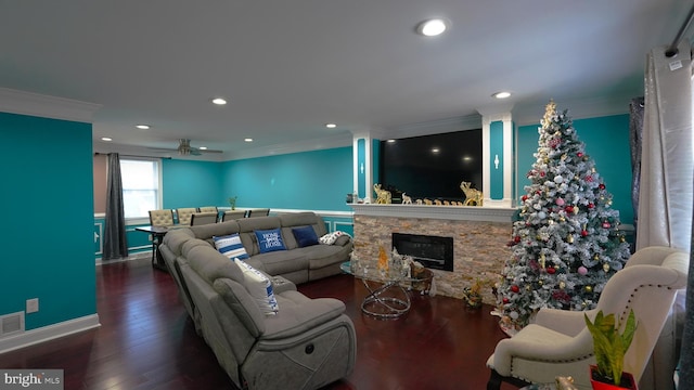 living room featuring dark hardwood / wood-style flooring, a stone fireplace, ceiling fan, and ornamental molding