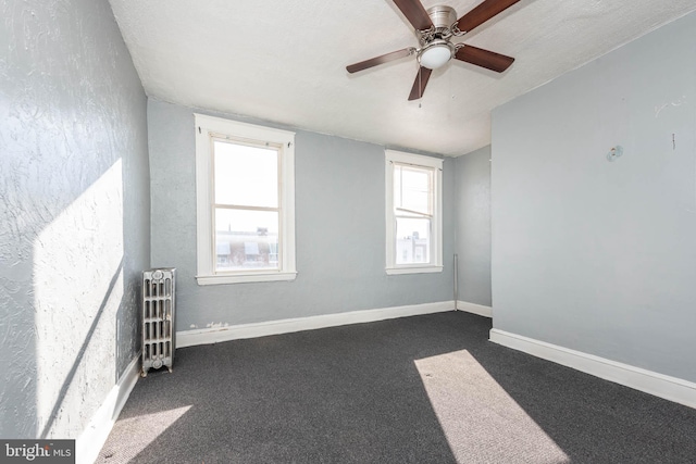 empty room featuring radiator, ceiling fan, dark carpet, and a textured ceiling