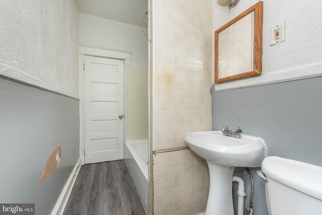 bathroom featuring hardwood / wood-style flooring, tile walls, and toilet