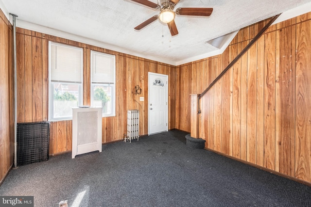 miscellaneous room with wood walls, ceiling fan, dark carpet, and a textured ceiling