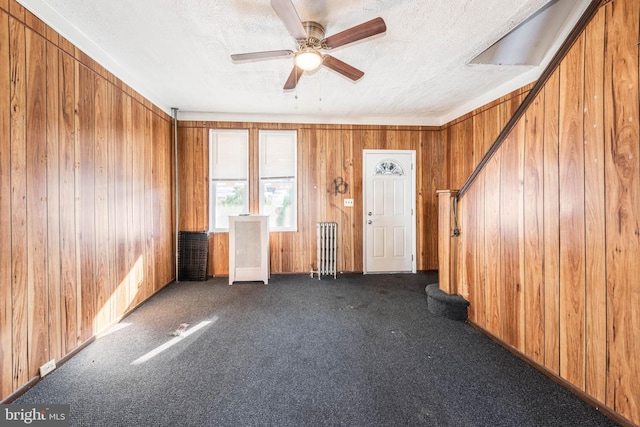 carpeted spare room with radiator heating unit, a textured ceiling, ceiling fan, and wood walls