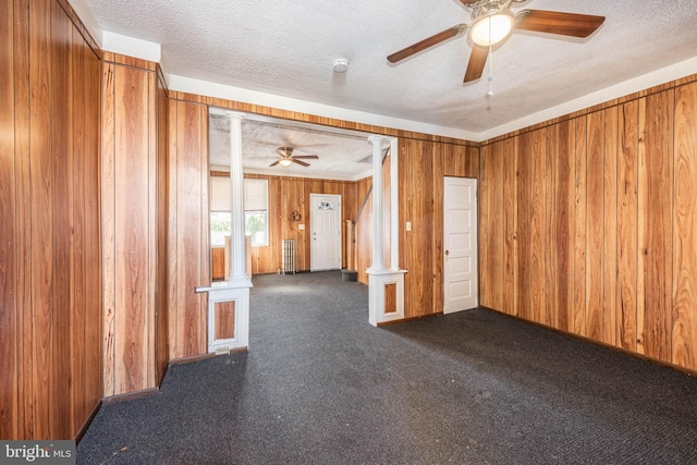 carpeted spare room with a textured ceiling, decorative columns, ceiling fan, and wooden walls