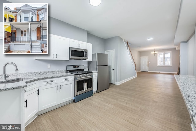 kitchen with light stone countertops, stainless steel appliances, sink, an inviting chandelier, and white cabinetry