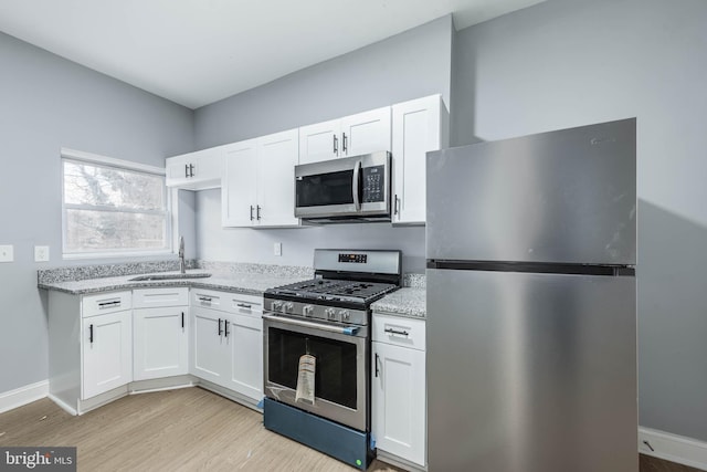 kitchen featuring white cabinets, appliances with stainless steel finishes, light stone counters, and sink