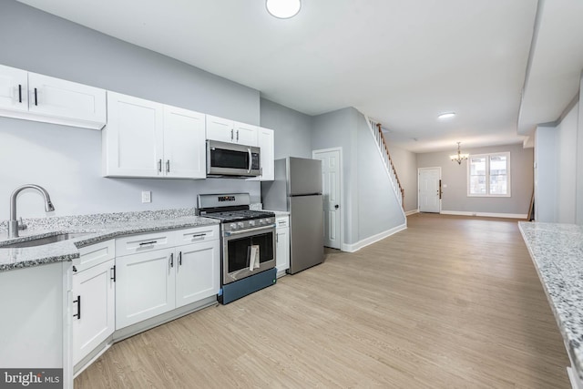 kitchen featuring appliances with stainless steel finishes, light stone counters, sink, a notable chandelier, and white cabinetry