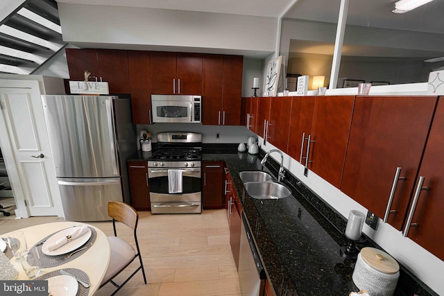 kitchen featuring stainless steel appliances, light hardwood / wood-style flooring, dark stone countertops, and sink