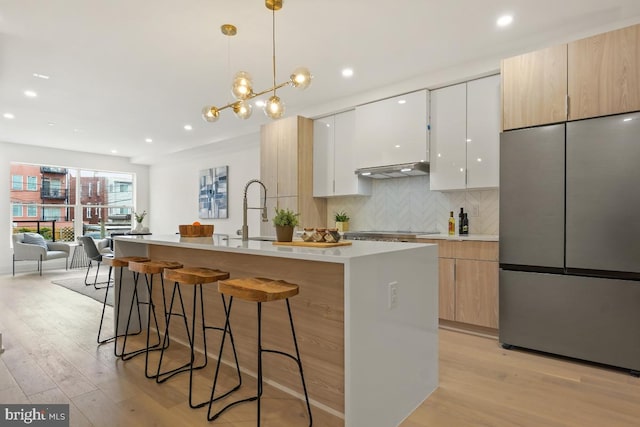 kitchen featuring stainless steel refrigerator, sink, tasteful backsplash, a kitchen island with sink, and white cabinets