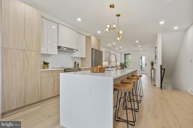 kitchen featuring stainless steel fridge, a breakfast bar, ventilation hood, hanging light fixtures, and an island with sink