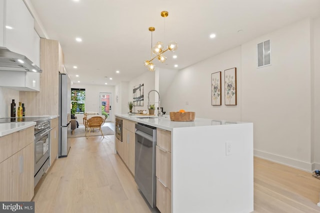 kitchen featuring sink, an island with sink, decorative light fixtures, light brown cabinetry, and appliances with stainless steel finishes