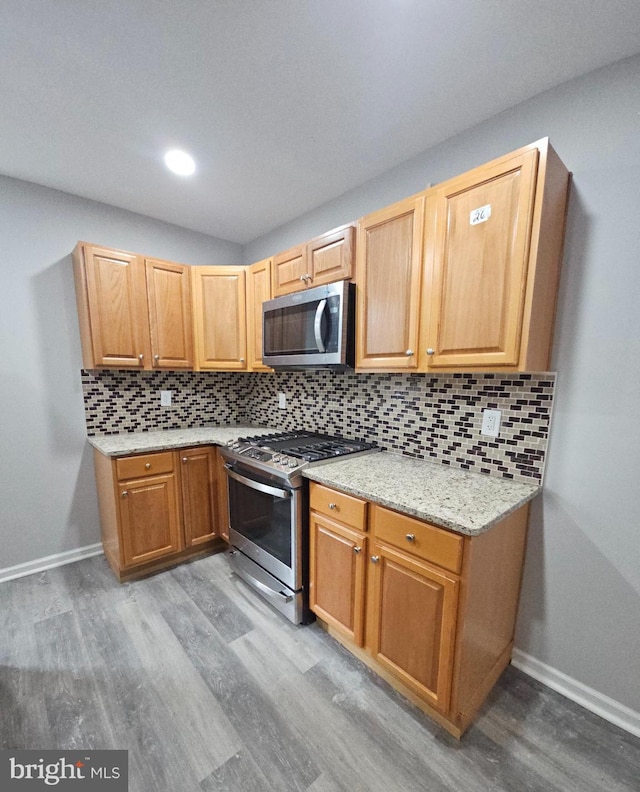 kitchen with tasteful backsplash, light stone countertops, light hardwood / wood-style floors, and appliances with stainless steel finishes