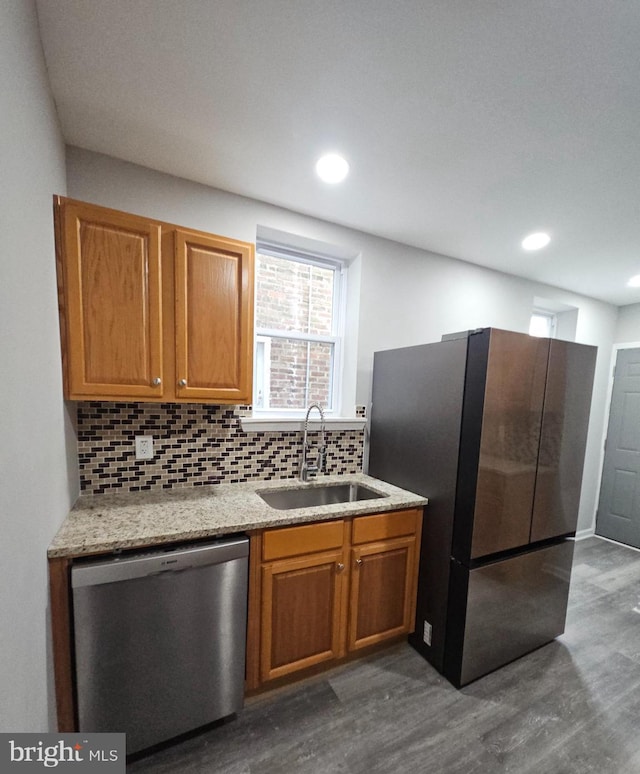 kitchen with light stone countertops, appliances with stainless steel finishes, tasteful backsplash, dark wood-type flooring, and sink