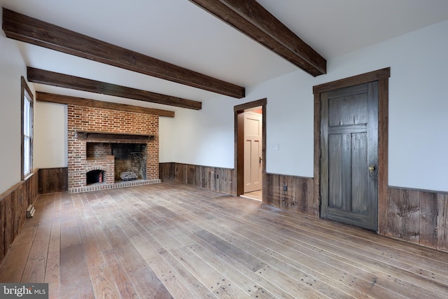 unfurnished living room with light hardwood / wood-style flooring, a brick fireplace, and wooden walls