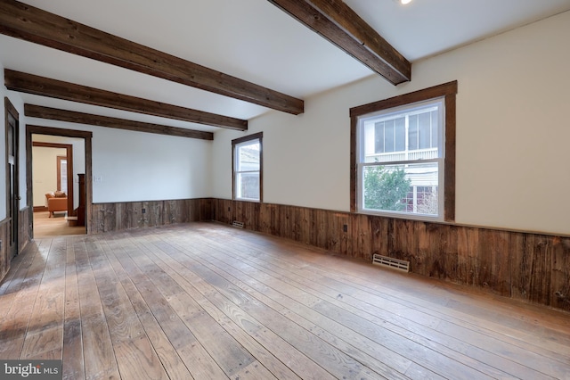 unfurnished room featuring beam ceiling, light wood-type flooring, and wood walls