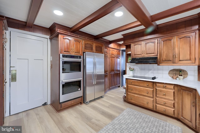 kitchen with beamed ceiling, appliances with stainless steel finishes, light wood-type flooring, and backsplash