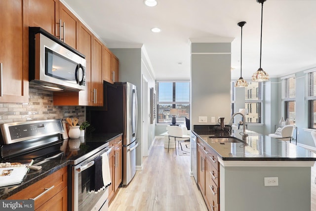 kitchen featuring a center island with sink, stainless steel appliances, ornamental molding, sink, and decorative light fixtures