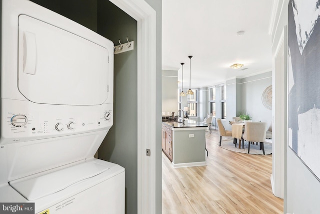 washroom with stacked washer and dryer, sink, light wood-type flooring, and ornamental molding