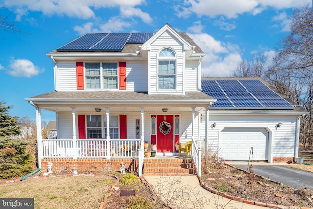 traditional-style home with aphalt driveway, roof with shingles, a porch, an attached garage, and roof mounted solar panels