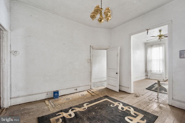 unfurnished room with ceiling fan with notable chandelier and light hardwood / wood-style flooring