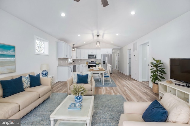 living room with sink, light wood-type flooring, ceiling fan, and vaulted ceiling