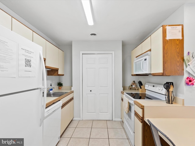 kitchen featuring sink, light tile patterned floors, white appliances, and cream cabinetry