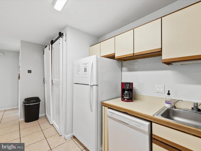 kitchen featuring white appliances, sink, a barn door, light tile patterned floors, and white cabinetry